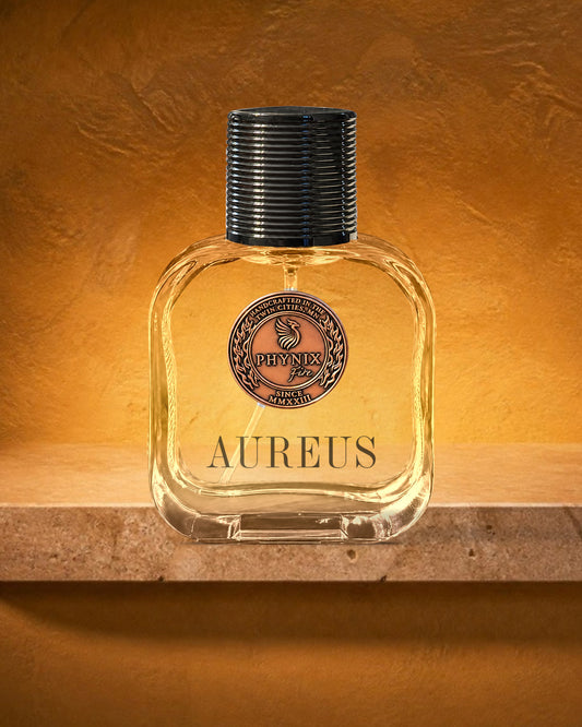 AUREUS 50 mL Parfum by Phynix Fire Studios — clear glass bottle with copper coin seal, ochre-gold plaster at golden hour on honey travertine