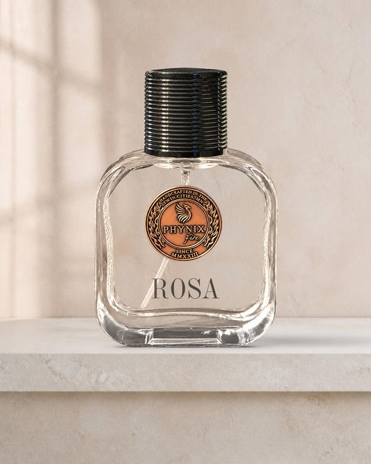 ROSA 50 mL Parfum by Phynix Fire Studios — clear glass bottle with copper coin seal, warm ivory plaster with window light on a pale stone ledge